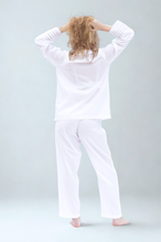 Load image into Gallery viewer, Person wearing white pajamas standing with hands behind head on a light gray background
