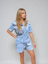 Load image into Gallery viewer, Woman wearing a light blue pajama set with a floral pattern on a gray background
