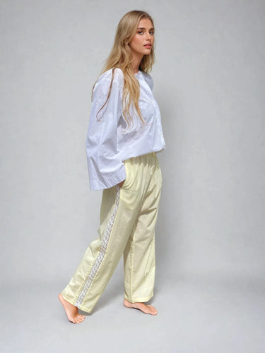 Woman wearing a white top and light buttermilk yellow trousers with a side stripe on a gray background