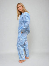 Load image into Gallery viewer, A woman modeling a light blue satin pajama set with a white floral pattern, standing against a neutral gray studio background.
