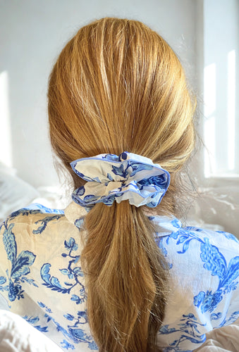 Person with blonde hair tied back with a blue and white scrunchie, wearing a blue and white patterned shirt.
