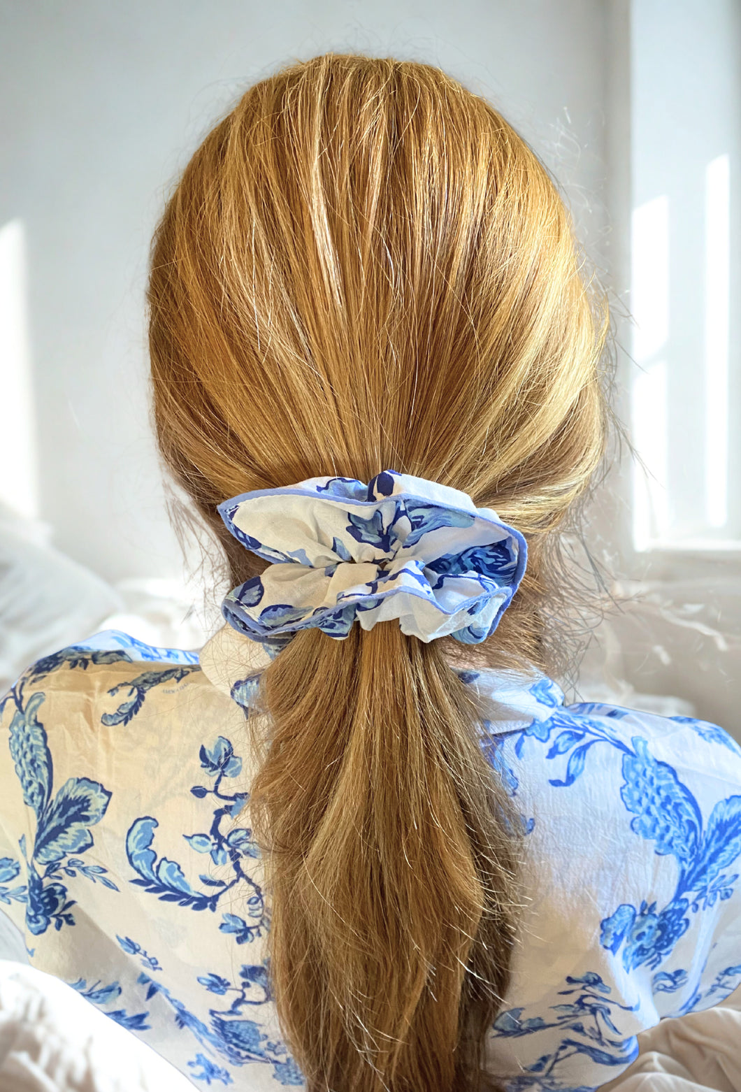 Person with blonde hair tied back with a blue and white scrunchie, wearing a blue and white patterned shirt.
