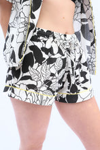 Load image into Gallery viewer, Black and white floral shorts with a yellow trim on a white background
